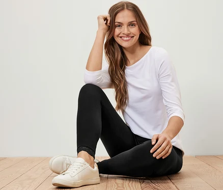 Une femme est assise sur un plancher en bois et porte un legging avec bord en dentelle, un t-shirt blanc à manches trois-quarts et des baskets blanches.