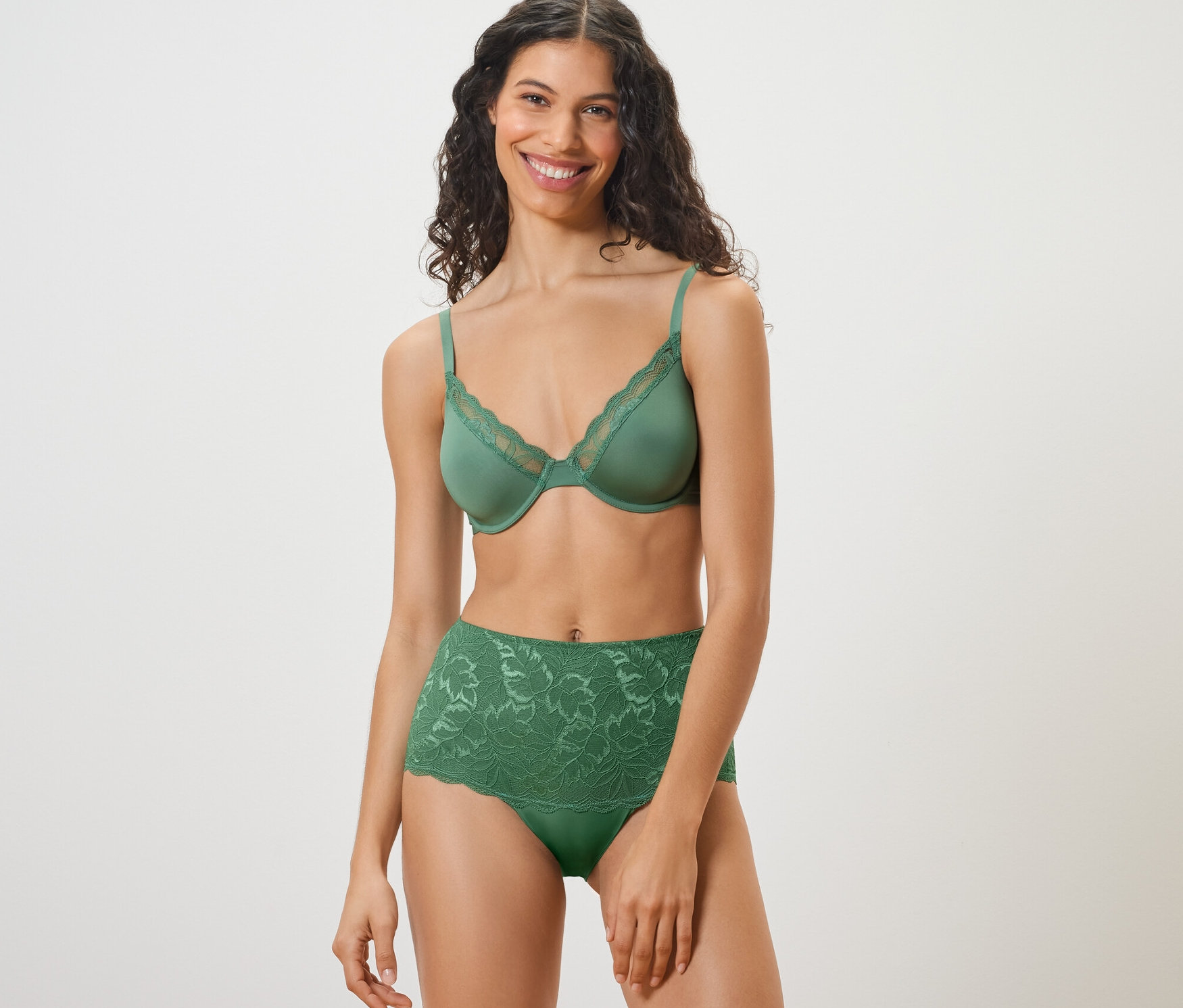 Une femme souriante porte un soutien-gorge vert et une culotte taille haute « light-shaping » verte.