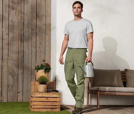 Un homme tient un arrosoir et porte un pantalon d'extérieur « Workwear ».
