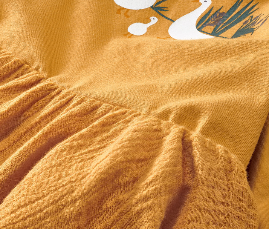 Gros plan sur une robe tissée jaune pour bébé avec un imprimé d'oies.