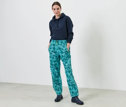 Une femme se tient debout, les mains dans les poches d'un pantalon de pluie imprimé.