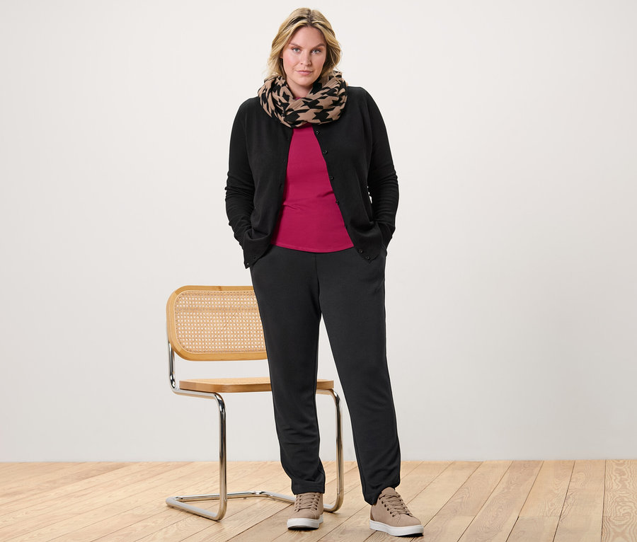 Une femme pose portant un t-shirt manches 3/4 rouge framboise, un cardigan en maille fine et un pantalon de jogging.
