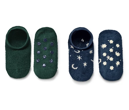 Deux paires de chaussons à enfiler. Une paire est verte avec des étoiles bleu foncé, l'autre bleu foncé avec des étoiles blanches et des lunes.
