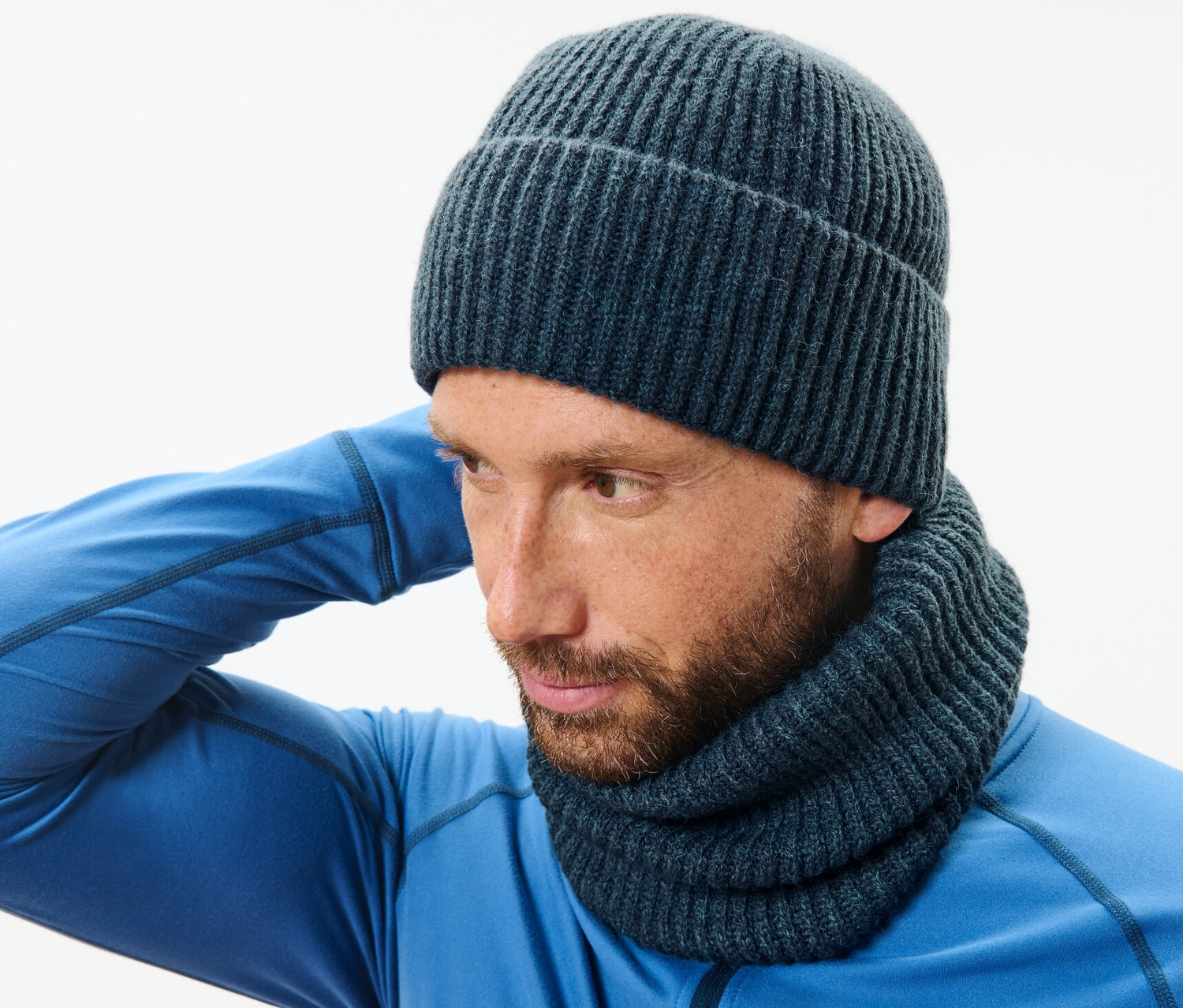 Un homme portant un pull bleu et une écharpe-tube en maille ajuste son bonnet.