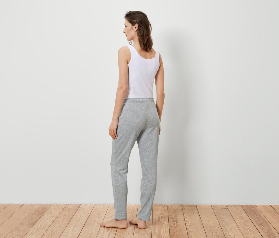 Une femme, vue de dos, porte un débardeur blanc et un pantalon de jogging gris.