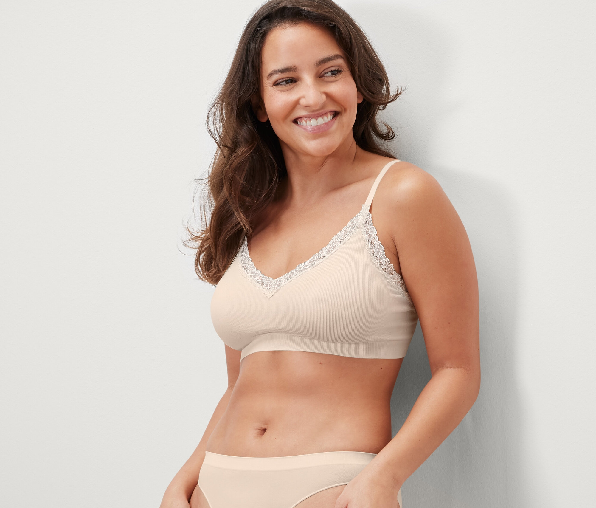 Une femme souriante porte une brassière seamless crème avec de la dentelle.