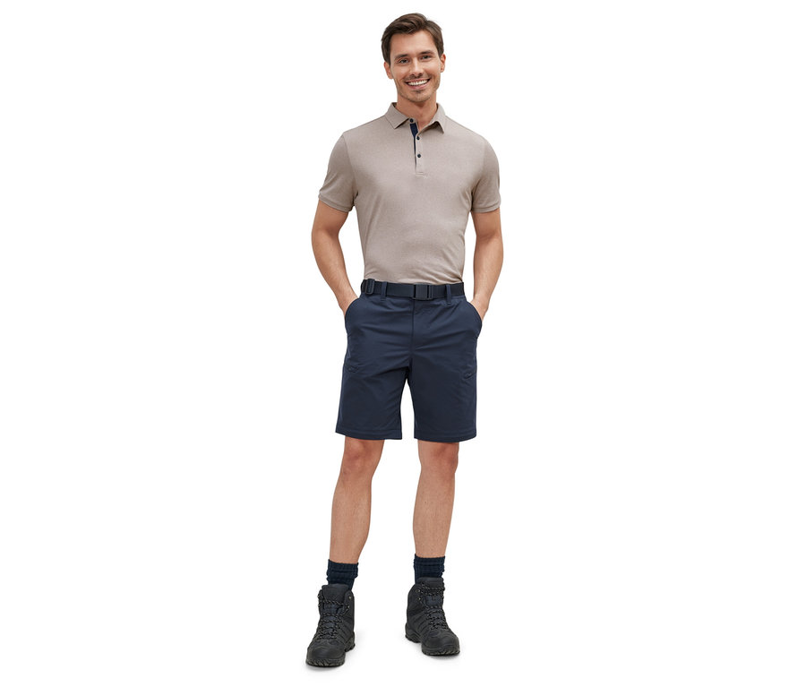 Un homme debout, les mains dans les poches, portant un polo beige et un pantalon technique 2 en 1 bleu.
