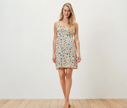 Une femme se tient debout, pieds nus, et porte une chemise de nuit à bretelles fines avec un imprimé floral.