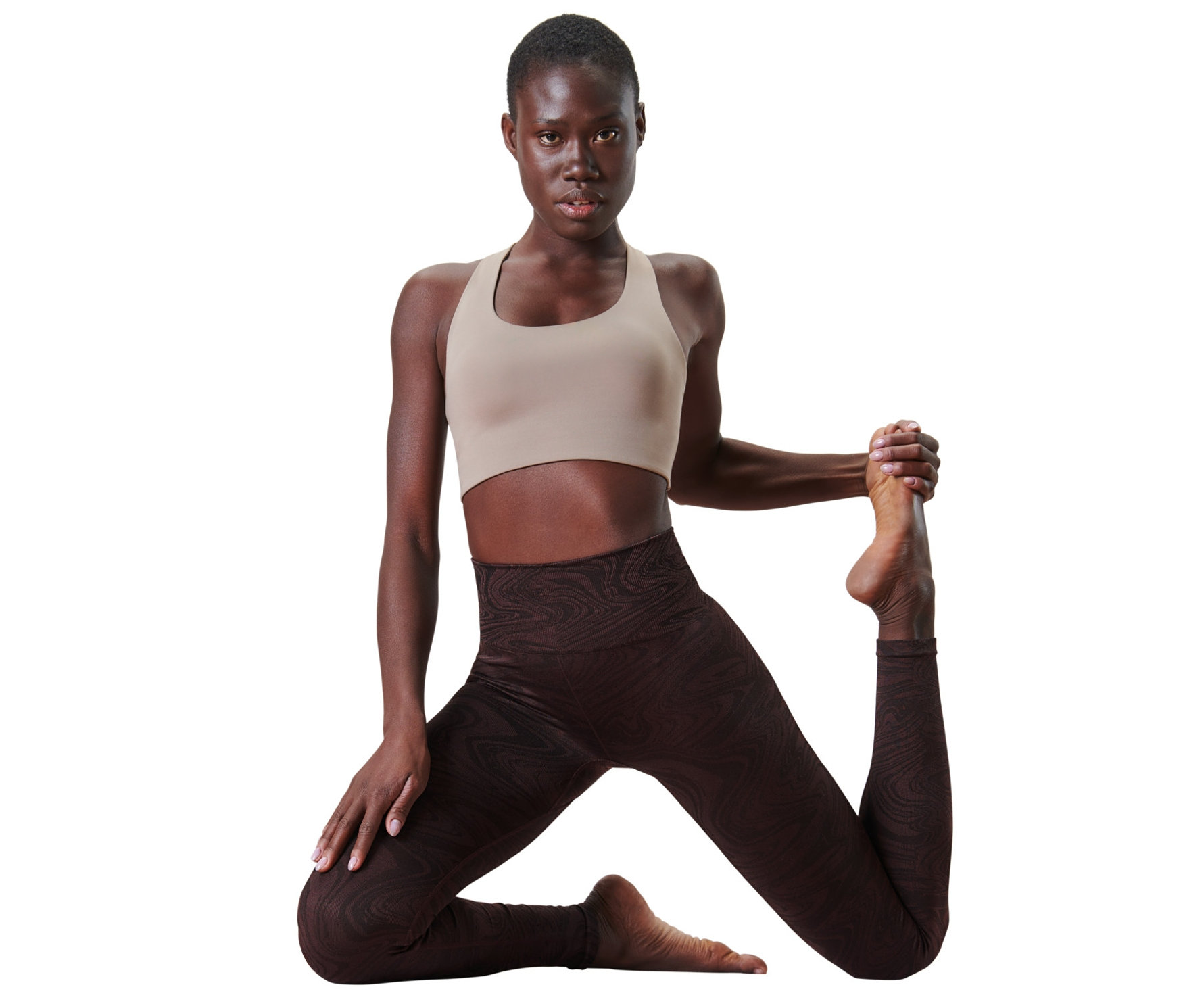 Femme en soutien-gorge de sport beige et legging sans coutures posant sur fond blanc.