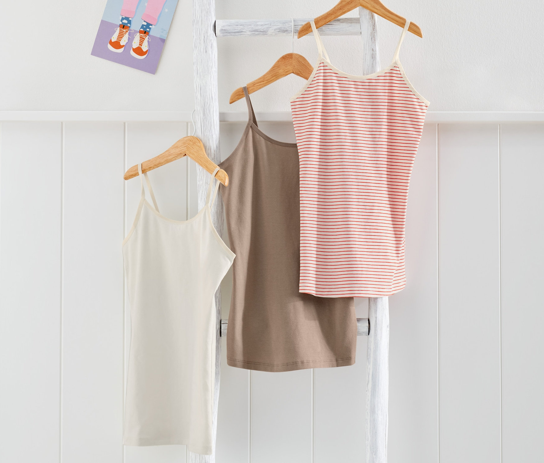 Trois maillots de corps enfant suspendus à une échelle blanche.