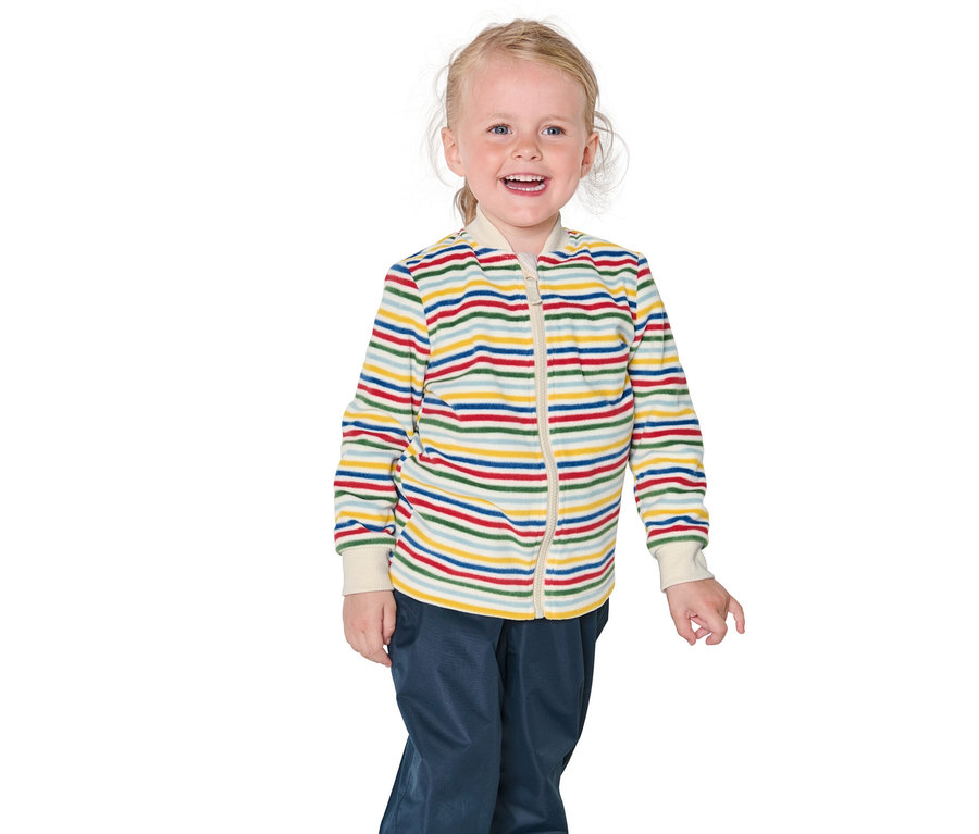 Une fillette blonde souriante porte une veste rayée et un pantalon bleu.