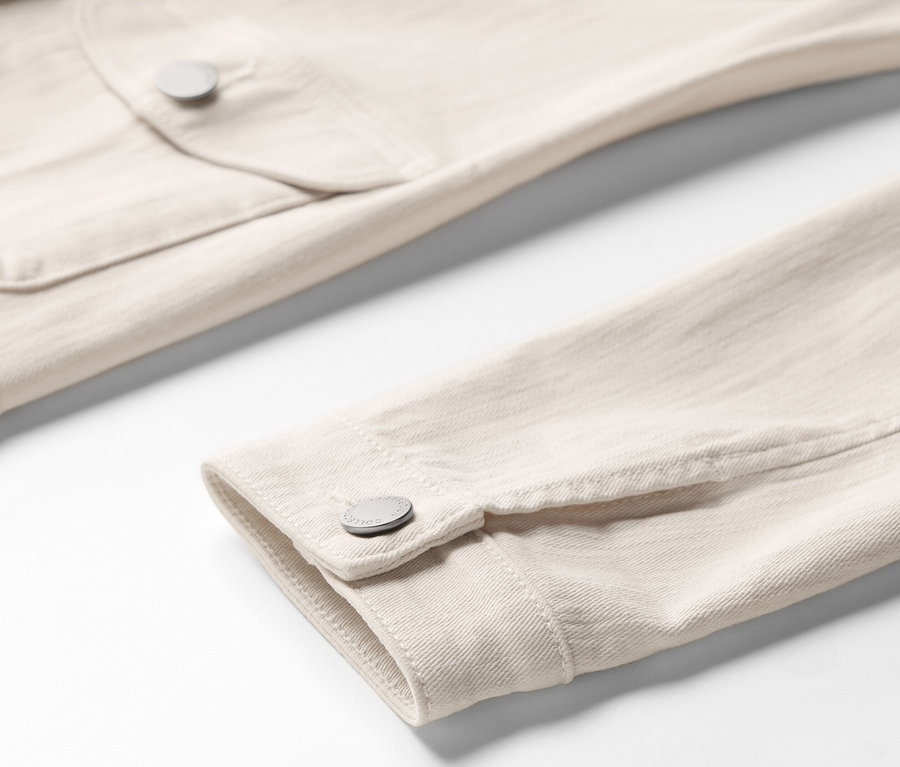 Gros plan sur une veste en jean beige clair avec des poches cargo, montrant une poche de poitrine et un poignet de manche.