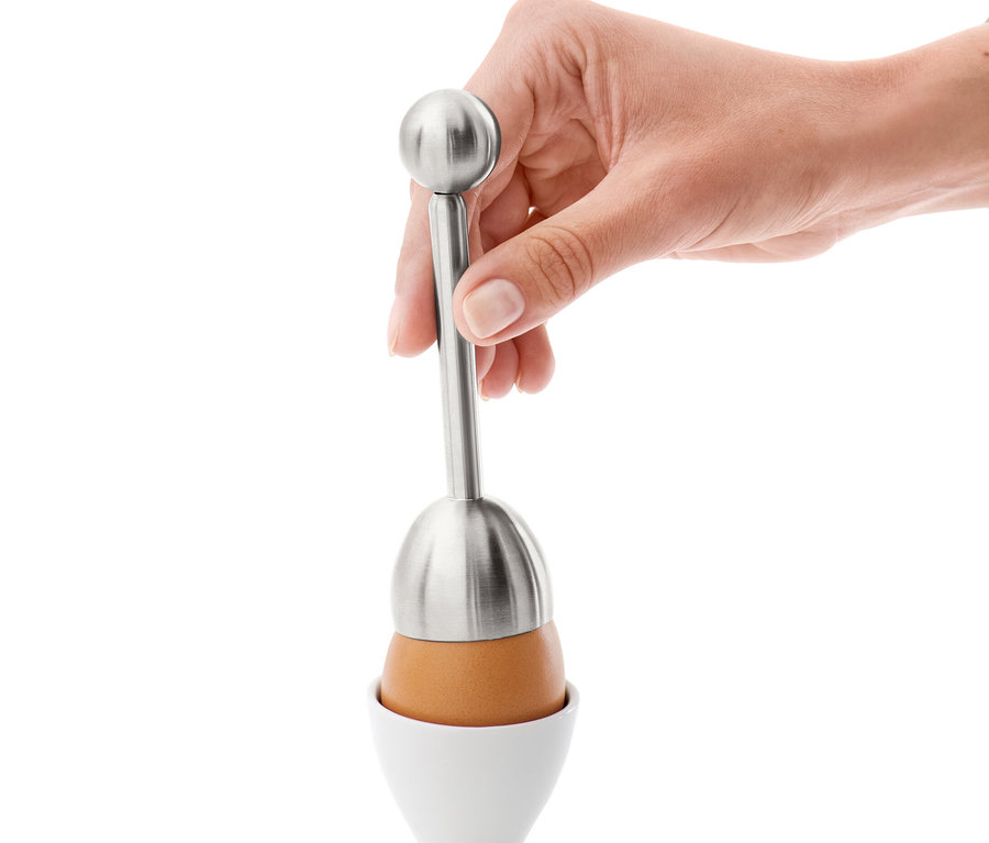 Une main utilise un coupe-œuf sur un œuf dans un coquetier blanc.