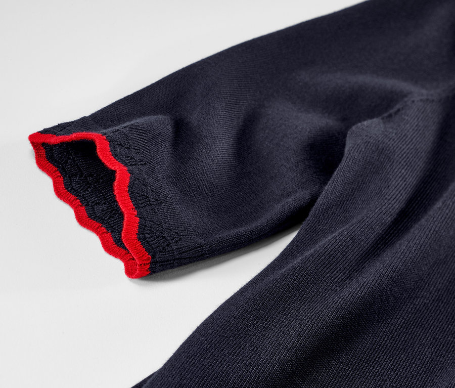 Gros plan sur un pull en maille fine bleu foncé avec une bordure rouge.