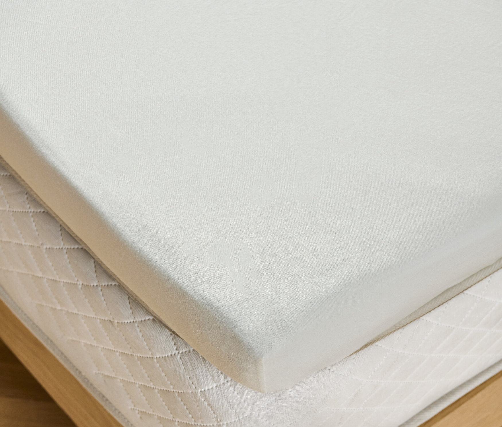 Gros plan d'un drap-housse blanc cassé taille normale pour topper sur un matelas sur un cadre en bois.