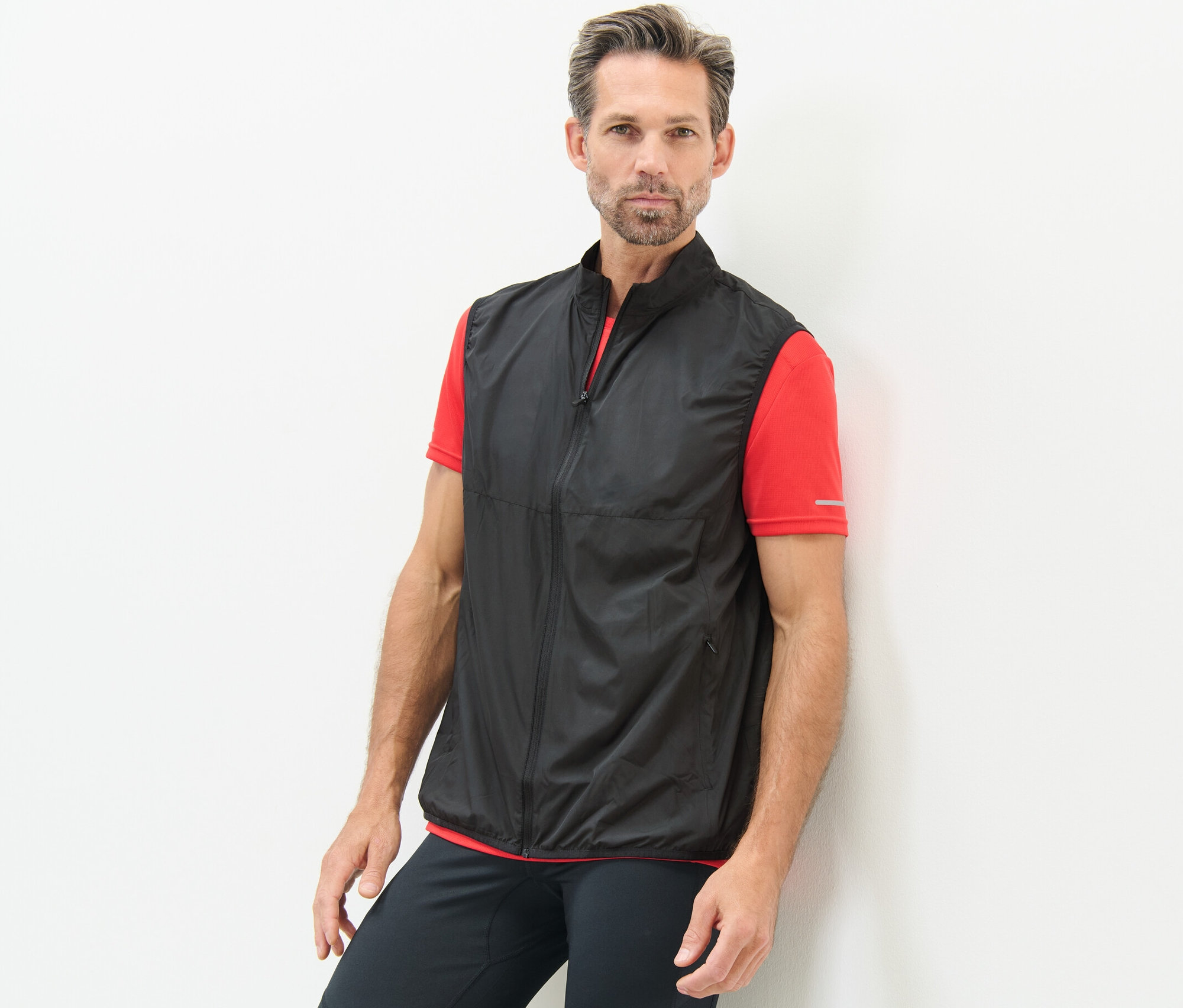 Un homme appuyé contre un mur porte un gilet technique sans manches.