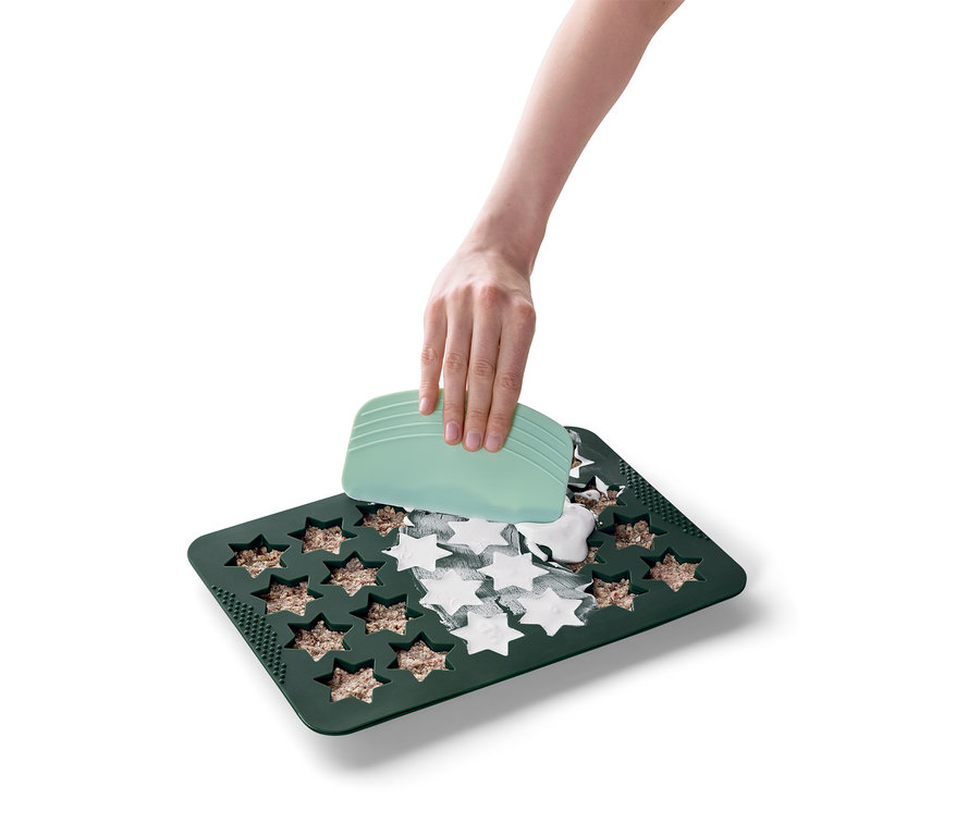 Une main utilise une spatule verte pour étaler une substance blanche dans un moule de cuisson vert en forme d'étoile.
