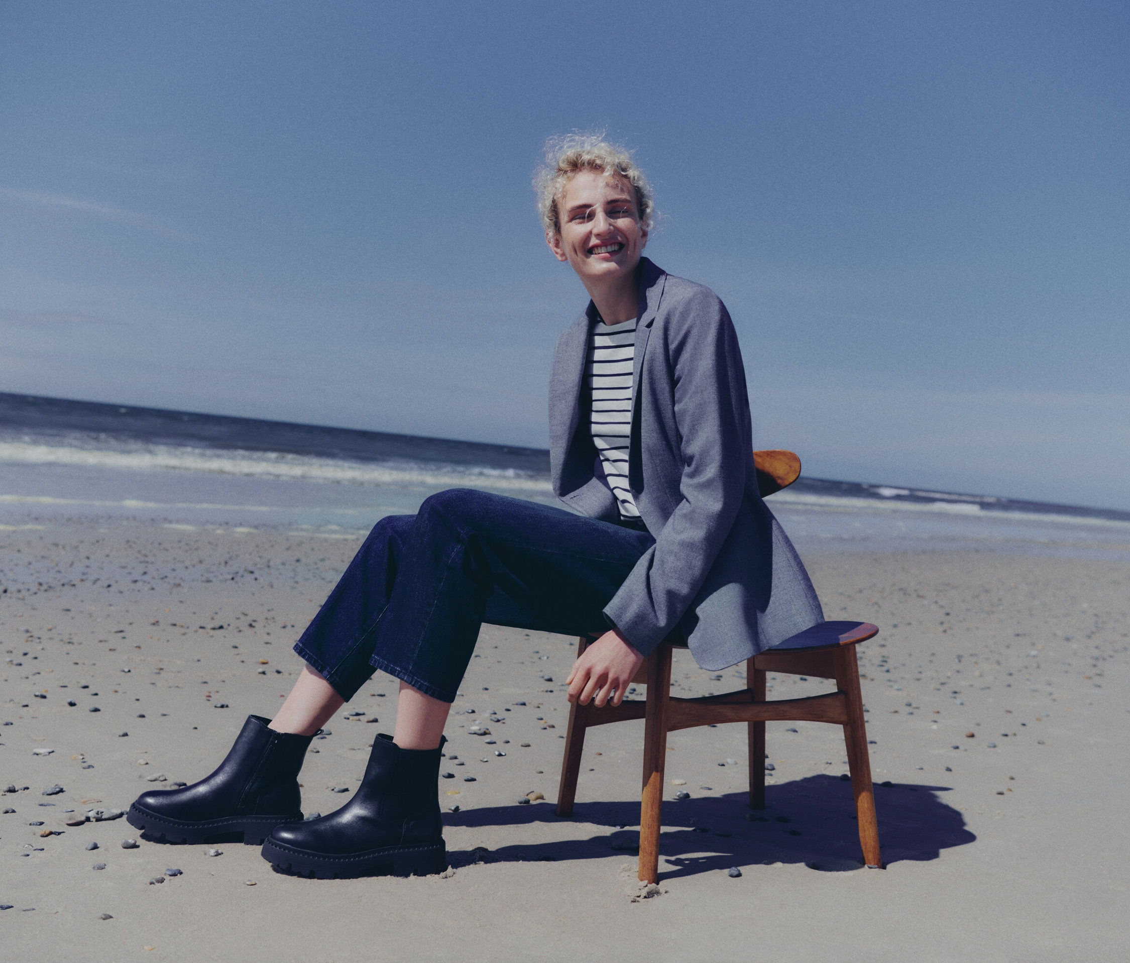 Une femme assise sur une chaise à la plage portant des bottines noires Tom Tailor à semelle épaisse.
