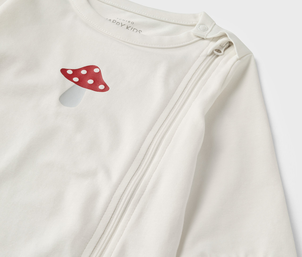 Gros plan sur un pyjama bébé rose et blanc avec une illustration de champignon et une fermeture éclair.