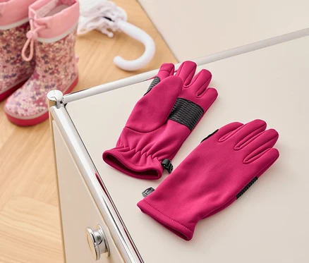 Une paire de gants roses est posée sur une table crème à côté de bottes en caoutchouc roses pour enfants et d'un parapluie blanc.