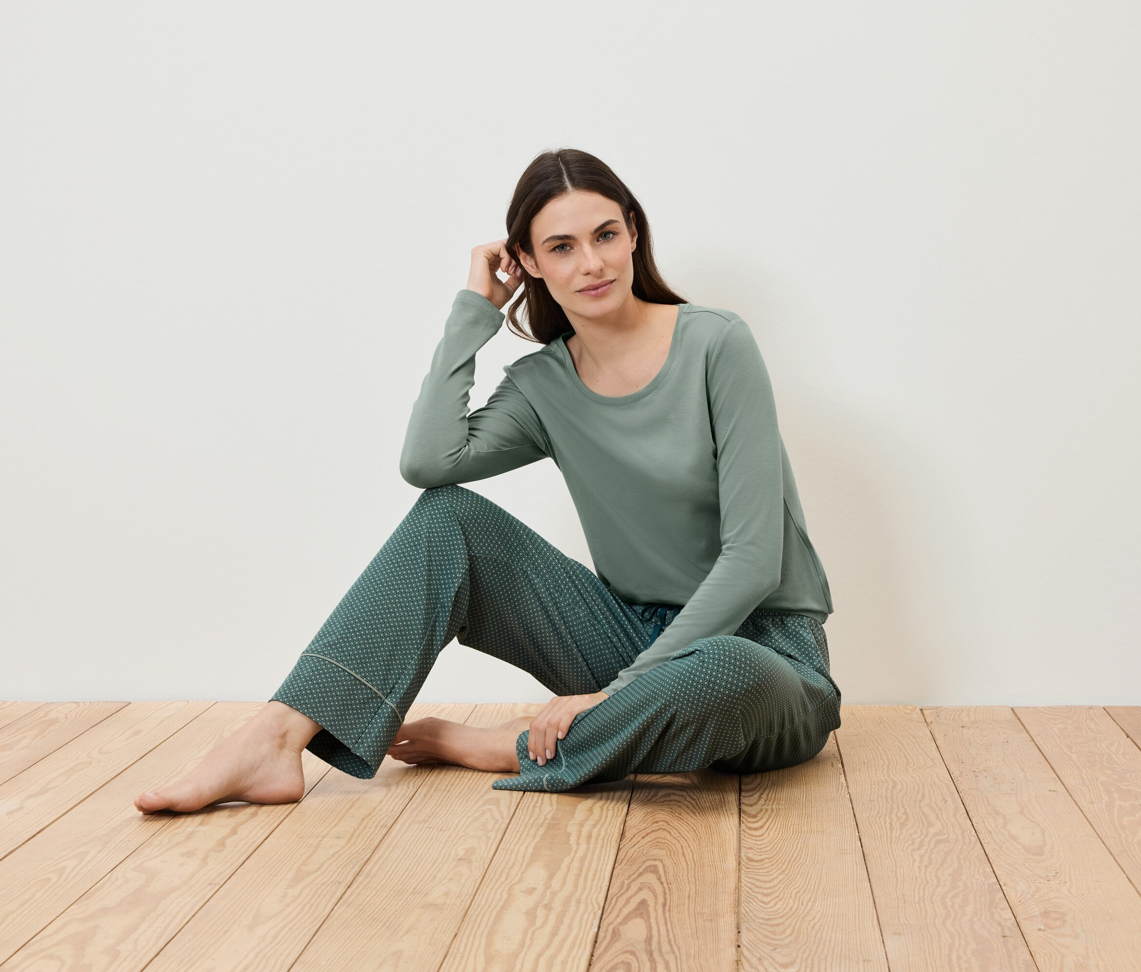 Une femme est assise sur un plancher en bois et porte un pyjama vert.
