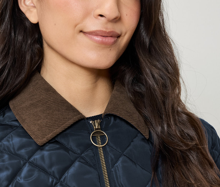 Gros plan d'une veste matelassée pour femme avec un col en velours côtelé marron et une fermeture éclair dorée.