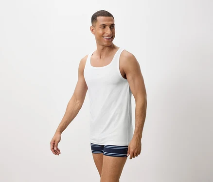 Un homme souriant porte un débardeur blanc et un boxer bleu rayé.