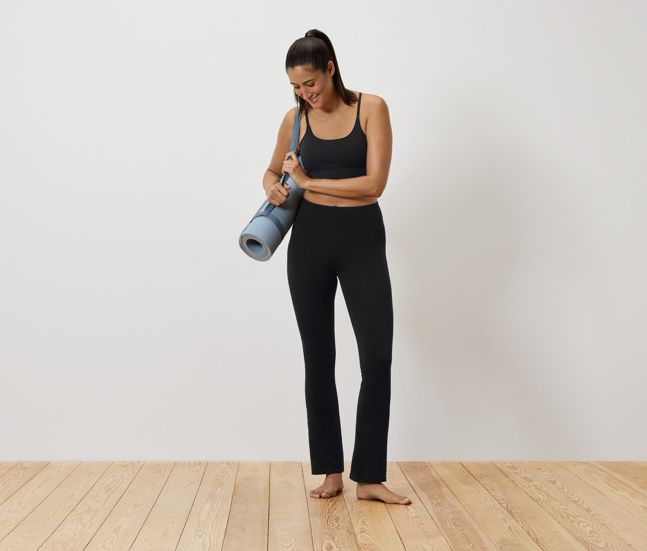 Femme en tenue de sport noire tenant un tapis de yoga.