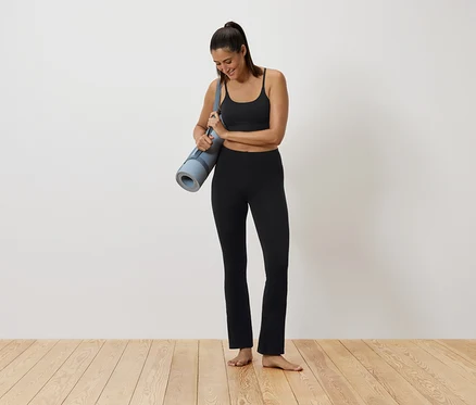 Femme en tenue de sport noire tenant un tapis de yoga.