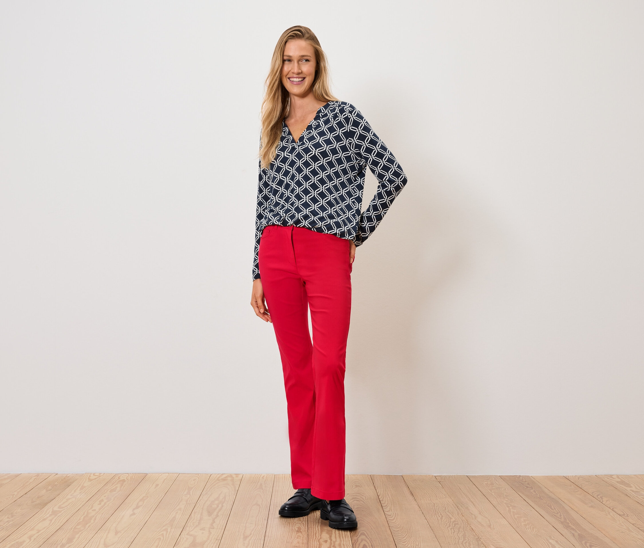 Une femme portant un haut bleu et blanc et un pantalon rouge se tient sur un plancher en bois.