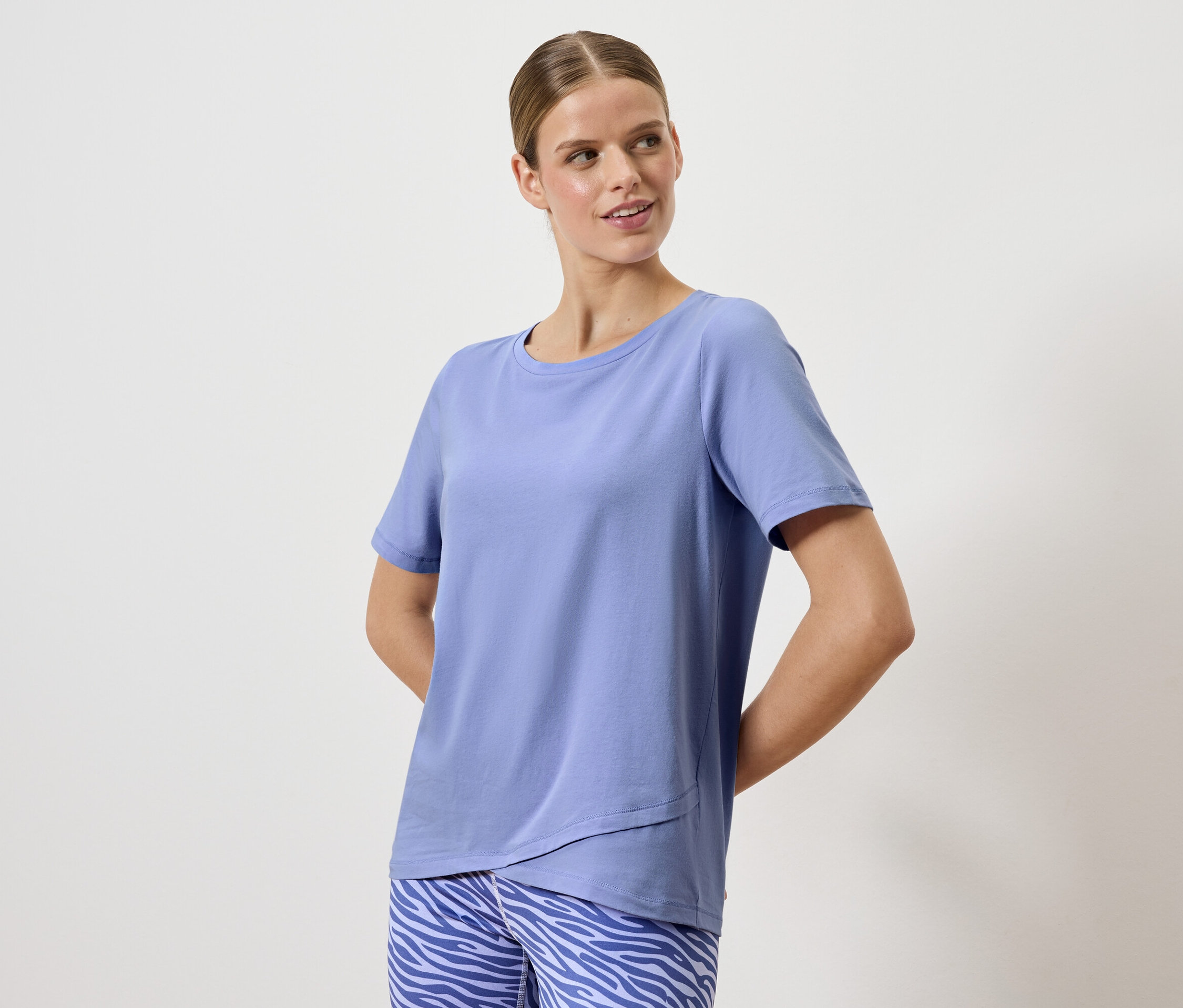 Femme posant dans un t-shirt bleu et un pantalon à motif animalier.