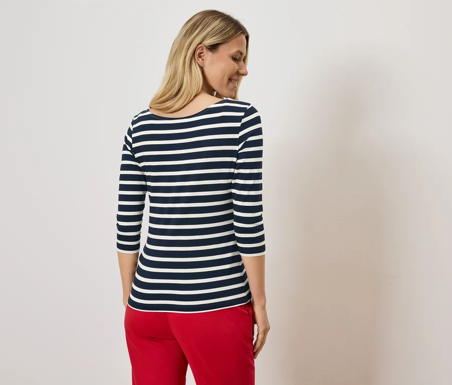 Femme blonde portant un t-shirt rayé bleu et blanc et un pantalon rouge.