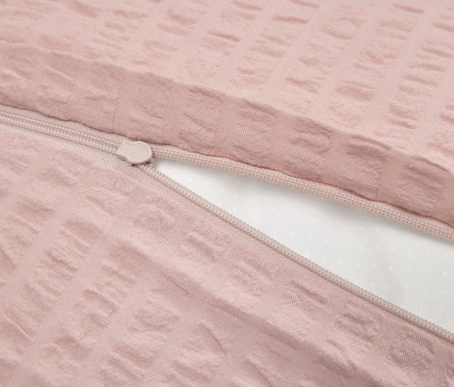 Gros plan d'une housse de couette rose texturée avec une fermeture éclair partiellement ouverte, révélant l'intérieur blanc.