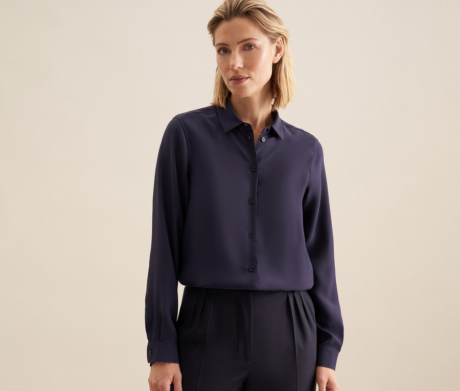Une femme porte un chemisier en viscose Seidensticker bleu marine foncé et un pantalon foncé.