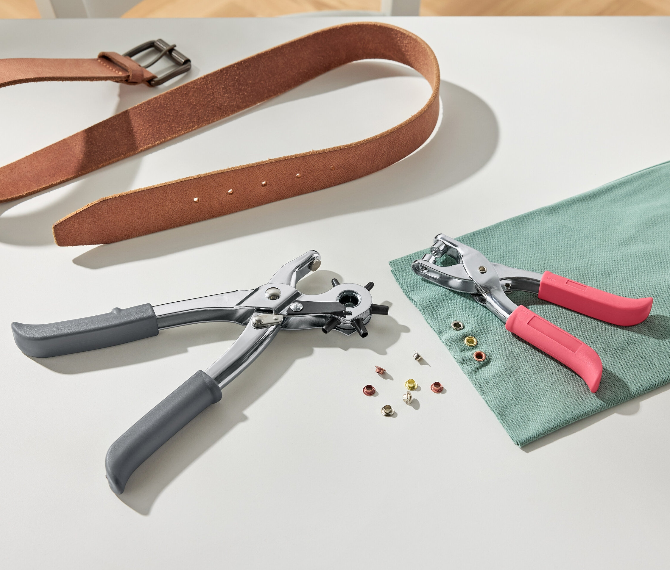 Une ceinture en cuir marron et une pince à perforer et à river sur un fond blanc.