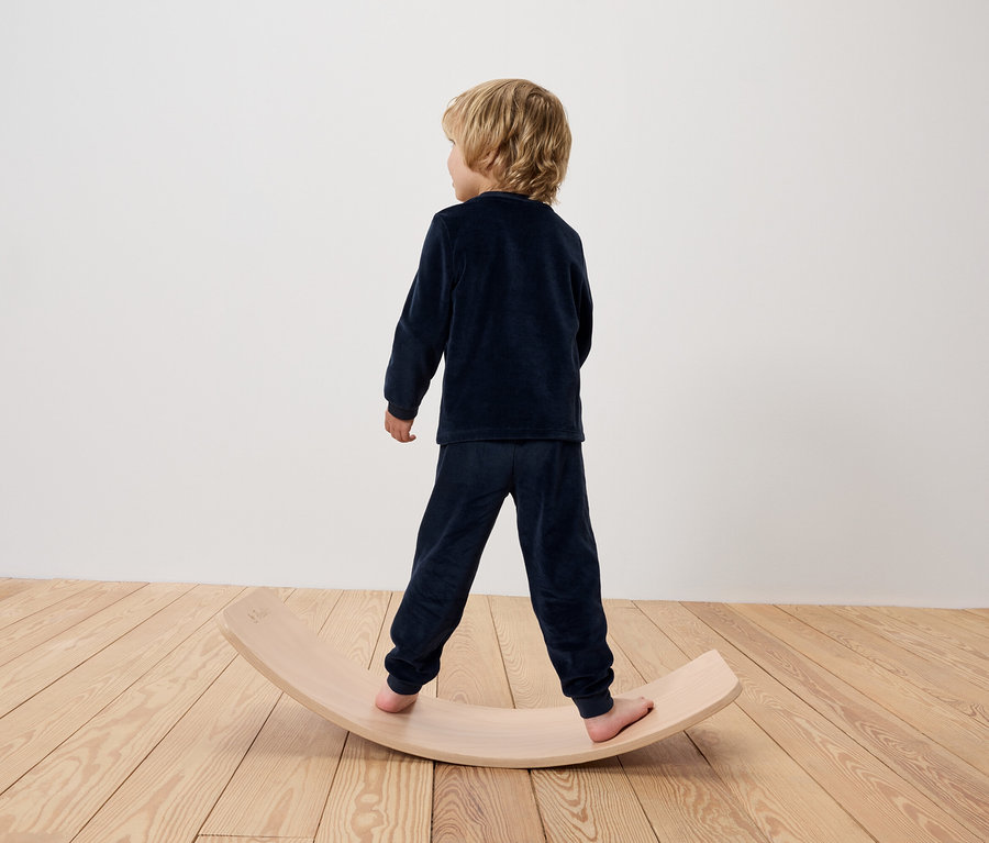Un garçon en pyjama bleu se tient sur une planche d'équilibre en bois.