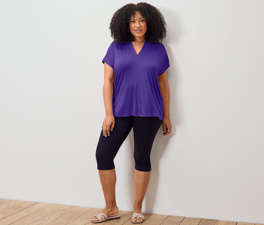 Femme posant en blouse violette avec encolure en V et pantalon 3/4 stretch noir.