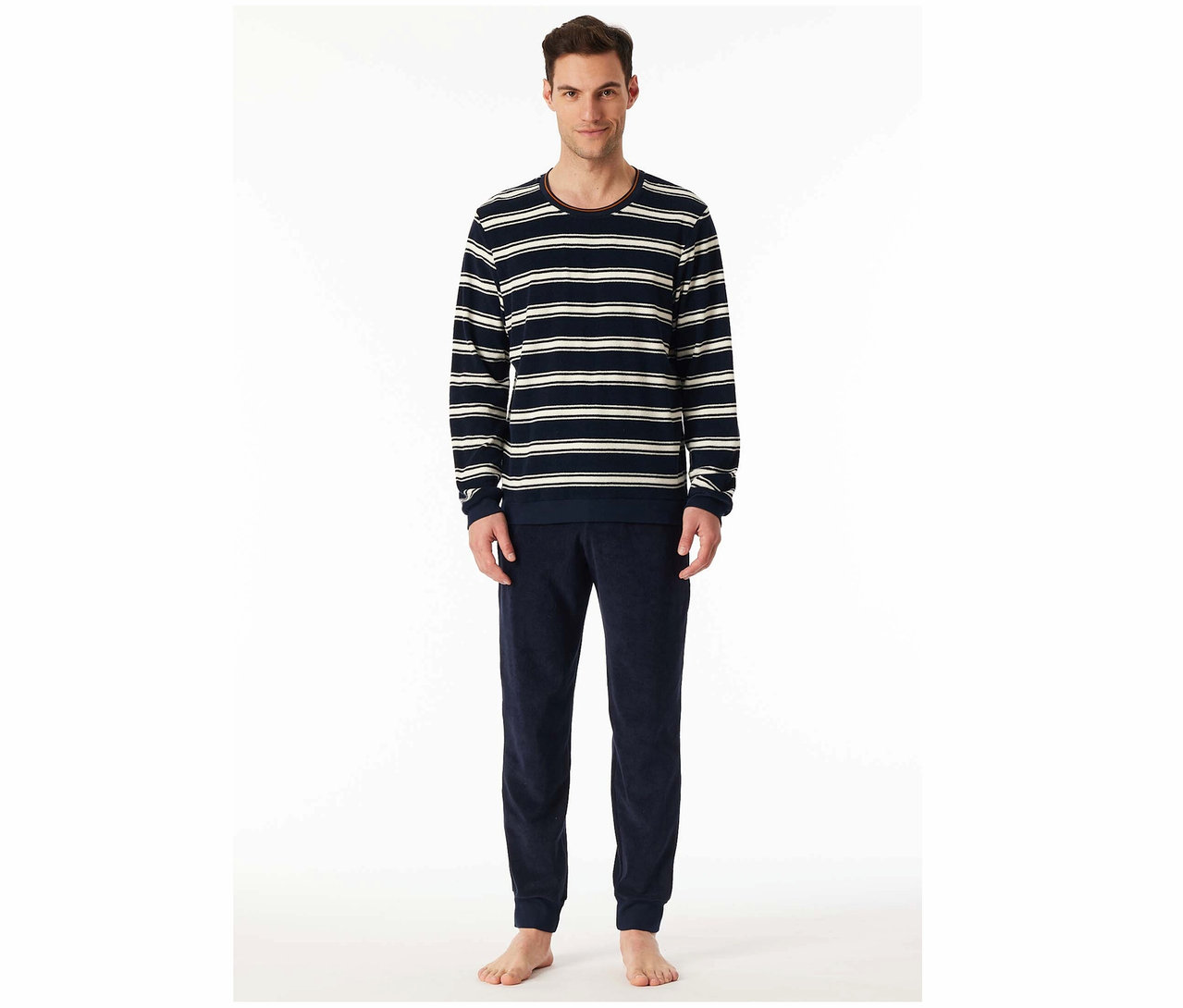 Un homme debout porte un t-shirt rayé à manches longues et un pantalon de survêtement en velours bleu marine.