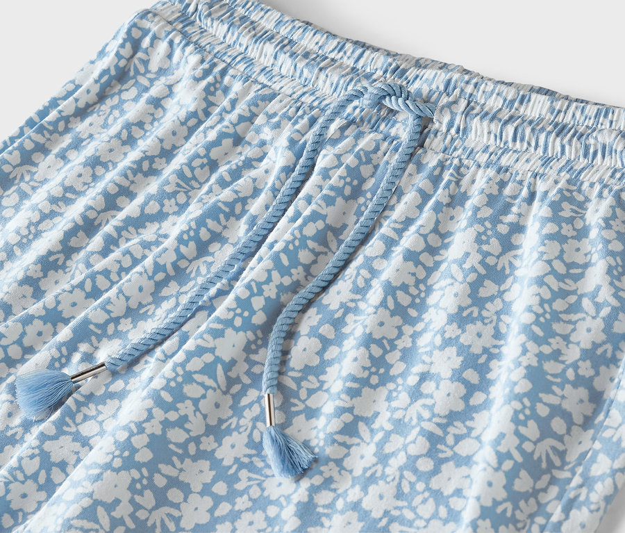 Détail d'un pantalon bleu clair avec un imprimé floral blanc, une taille élastique et un cordon de serrage bleu.