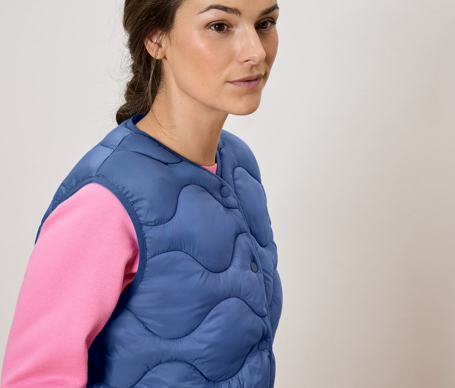 Femme portant un gilet matelassé bleu sur un haut rose.