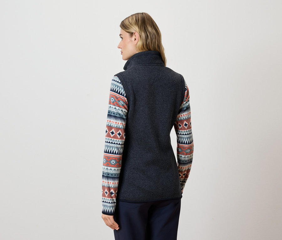 Une femme, dos à la caméra, porte une veste en polaire gris foncé et un pantalon bleu.