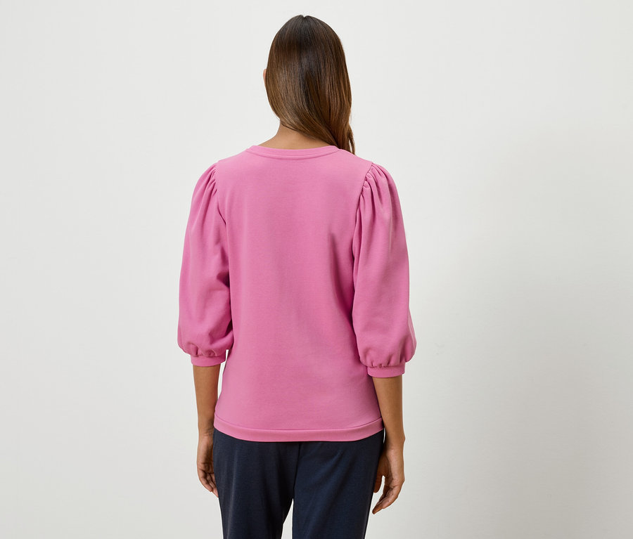 Une femme, vue de dos, porte un sweat-shirt rose à manches bouffantes trois-quarts.