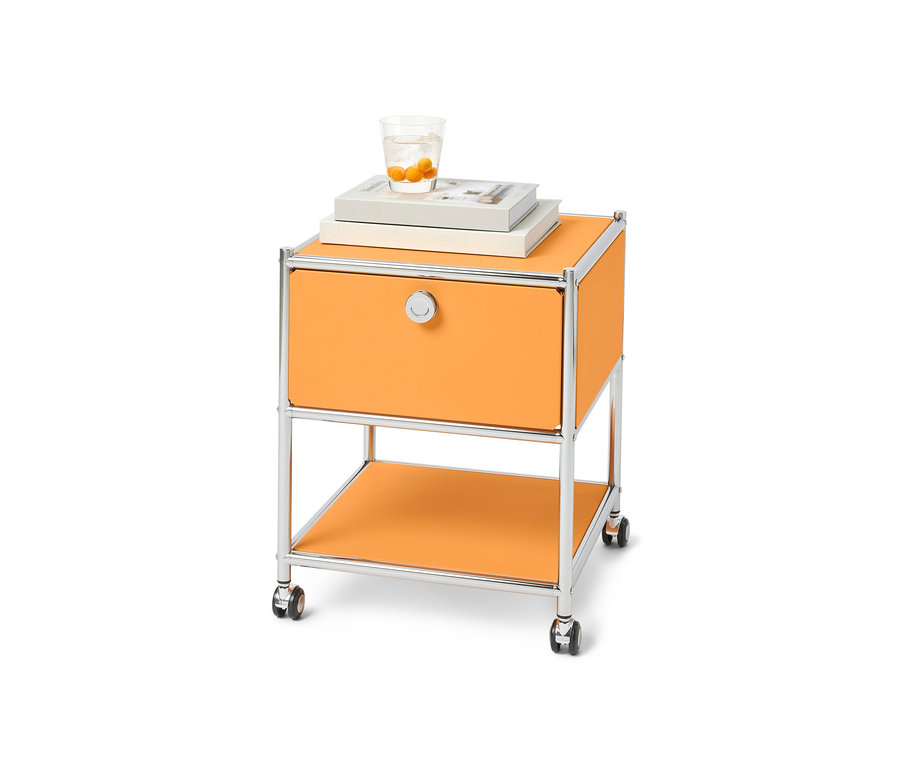 Table d’appoint orange avec tiroir en métal « CN3 » sur roulettes. Des livres et un verre d'eau sont posés sur la table.