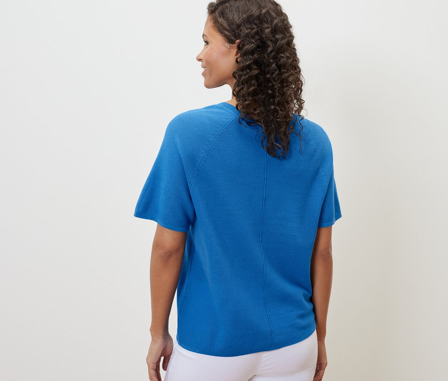 Une femme vue de dos portant un t-shirt en maille fine bleu cobalt et un pantalon blanc.