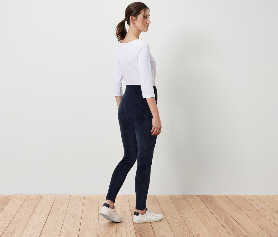 Femme en haut blanc et legging bleu en velours côtelé debout sur un plancher en bois.