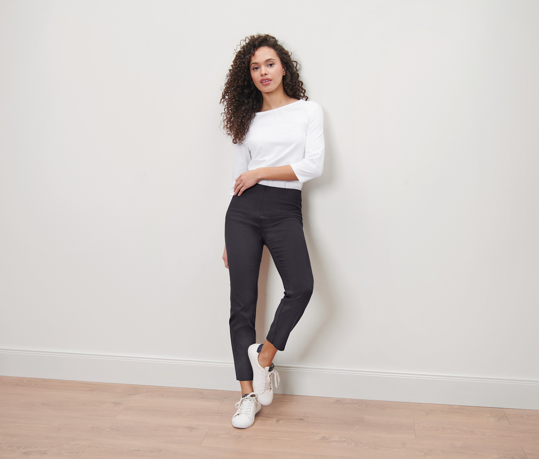Femme posant en pantalon stretch, haut blanc et baskets.