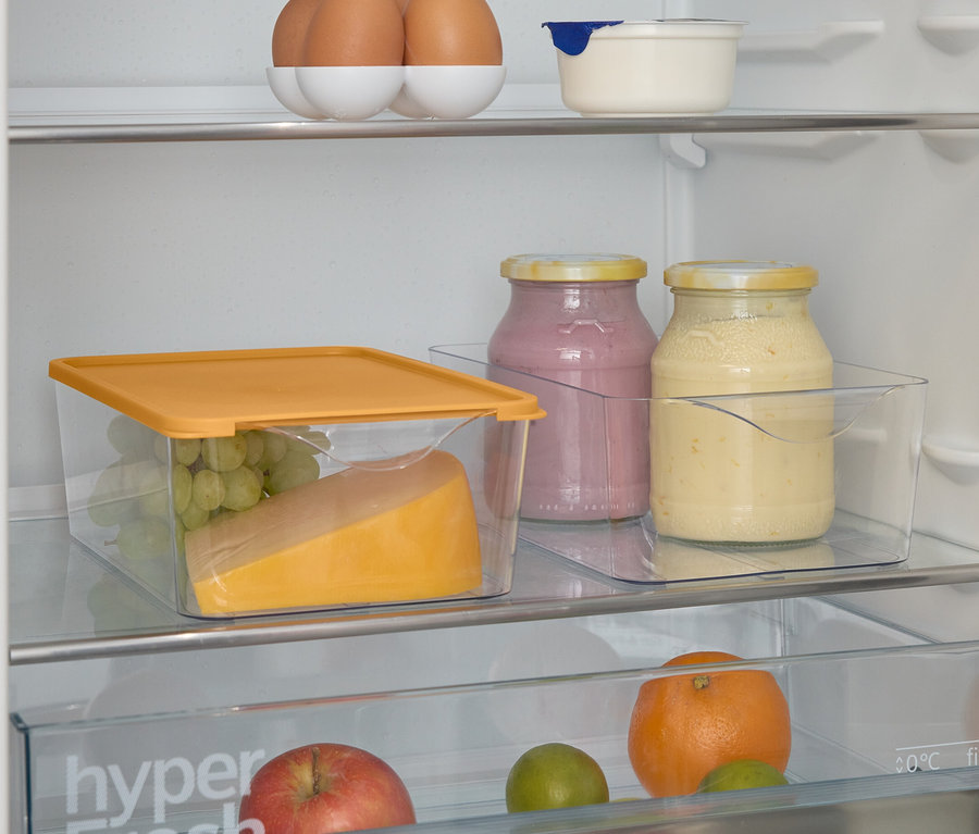 Vue de l'intérieur d'un réfrigérateur contenant des aliments. Des œufs en haut, des pots de confiture, du fromage et des raisins dans un récipient transparent en dessous.