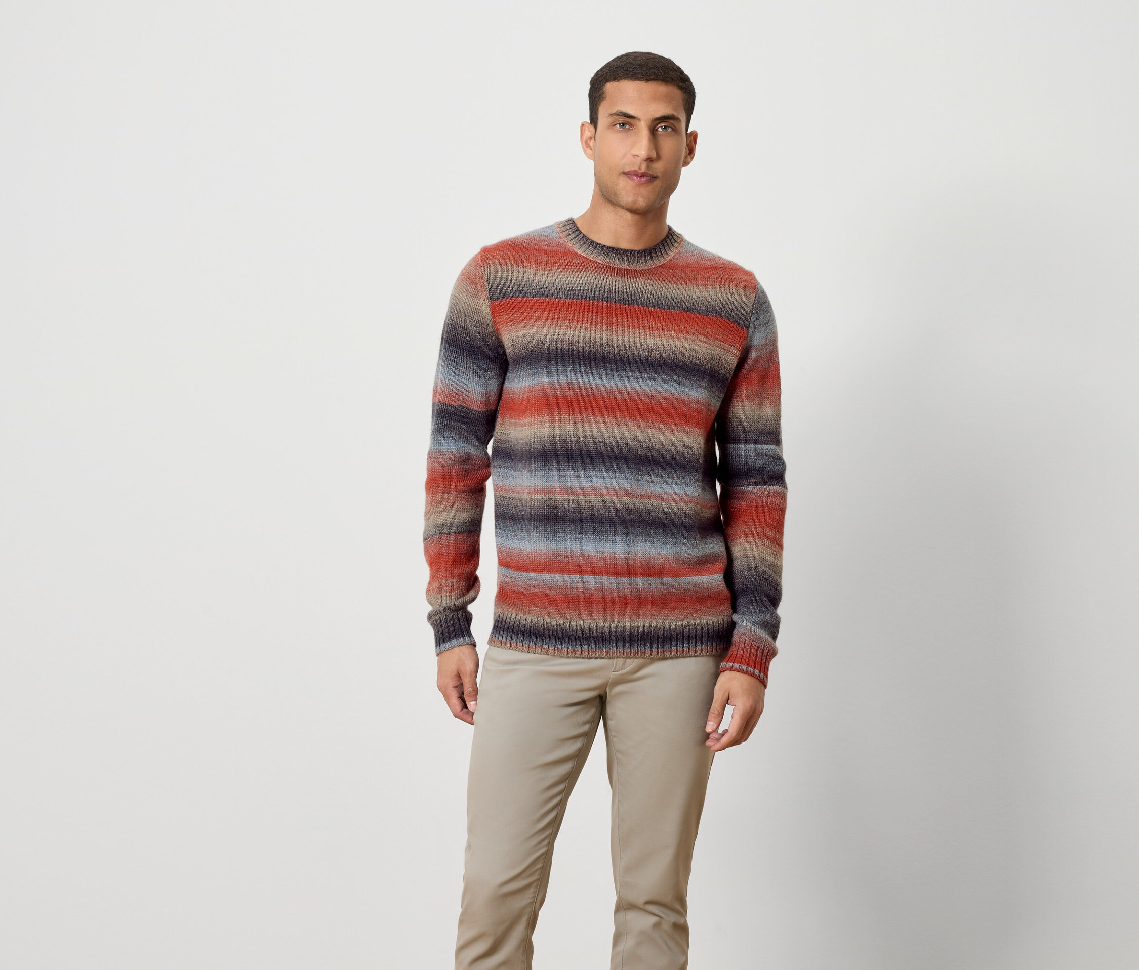 Un homme debout portant un pull rayé et un pantalon.