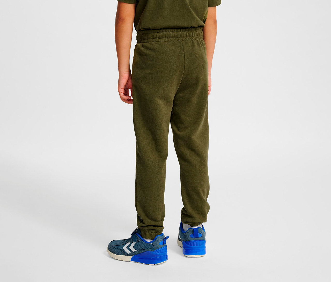 Garçon vu de dos portant un pantalon régulier HUMMEL HMLJR Base, vert et des chaussures bleues.