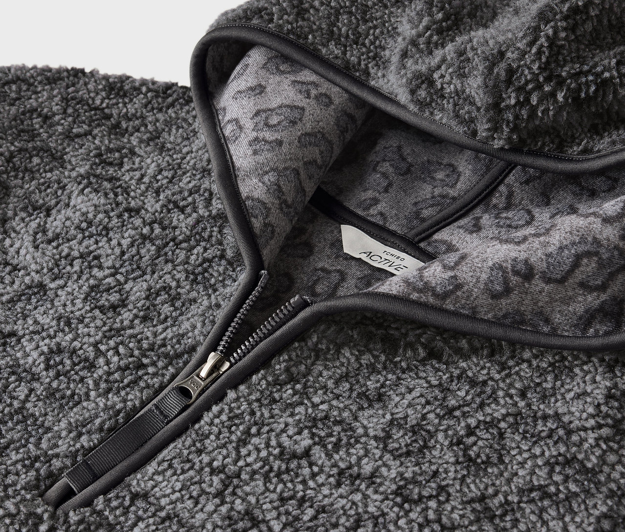 Gros plan sur un sweat à capuche gris en fausse fourrure avec fermeture éclair et motif animalier gris à l'intérieur de la capuche.